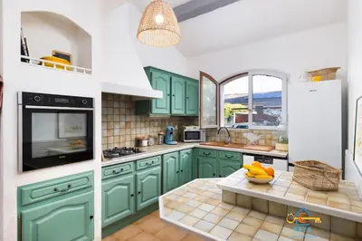 a kitchen with green cabinets and a bowl of fruit on a table at Maison Jade - Villa avec piscine - Barbecue - Calme in Narbonne