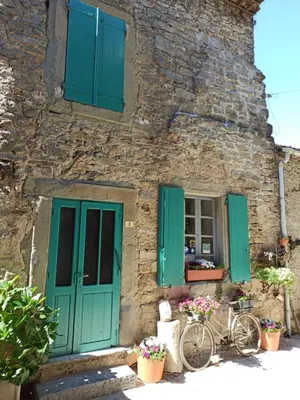 a stone house with green shutters and a bicycle outside at Gite les Volets Verts in Cesseras