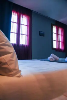a bedroom with a bed and two windows with red curtains at Hôtel du vieux pont in Mazères