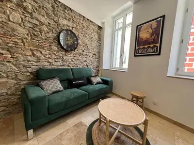 a living room with a green couch and a stone wall at Le Gîte Médiéval - Clim - Lave Linge - Cité in Carcassonne