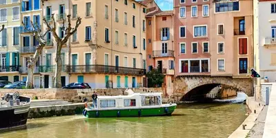 a green and white boat in a canal with buildings at You&Me hyper centre ville avec draps serviettes ménage final in Narbonne