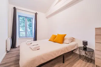 a white bedroom with a large bed with yellow pillows at La Petite Bastide in Carcassonne