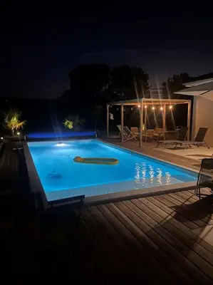 a blue swimming pool at night with a house at Maison charme et confort - piscine chauffée in Tarabel