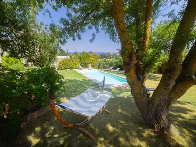 a chair sitting under a tree next to a swimming pool at Domaine des Périès - Chambres d'hôtes in Saint-Martin-Lalande