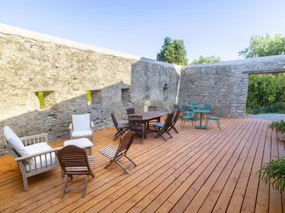 a wooden deck with chairs and tables and a stone wall at Domaine des Périès - Chambres d'hôtes in Saint-Martin-Lalande