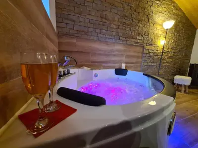 a bath tub with a glass of champagne and a glass of wine at Refuge Insolite avec balnéo privative en forêt in Pont-de-Larn