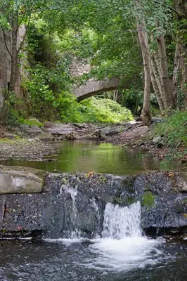a waterfall in a creek with a bridge in the background at Au Pont Romain Gites in Caunes-Minervois