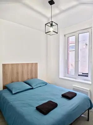 a bedroom with a bed with blue sheets and a window at Tour Est - T2 entre Cité Médiévale et Bastide in Carcassonne
