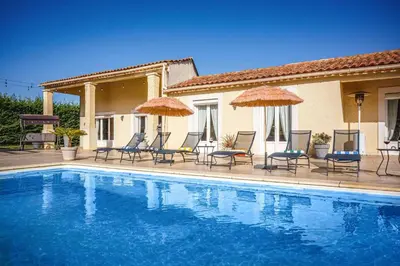 a pool with chairs and umbrellas next to a house at Villa Loupia by Villa Plus in Loupia