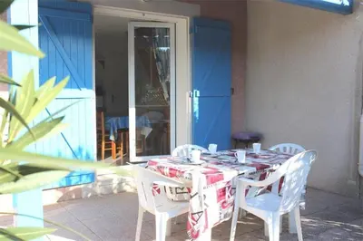 a table with white chairs and a blue door at Pavillon dans résidence avec piscine Grazel GA090-056 in Gruissan