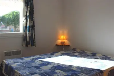 a bedroom with a bed and a lamp and a window at Pavillon dans résidence avec piscine Grazel GA090-056 in Gruissan