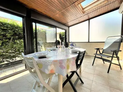 a dining room with a table and chairs and windows at Petit pavillon climatisé avec parking privé Grazel GN490-055 in Gruissan