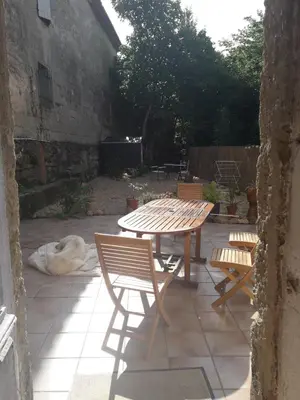 a patio with a table and two chairs and a dog at Maison Rose - Maison de village avec jardin privé, centre Capestang in Capestang
