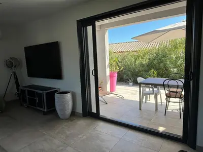 a sliding glass door to a patio with a table and a television at La Maison Laurier in Lézignan-Corbières