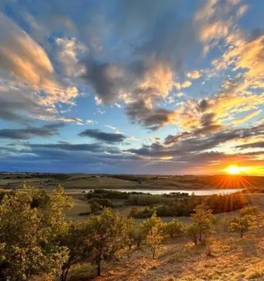 a sunset over a field with trees and a river at La bergerie - Paisible vue lac et montagne in Molleville
