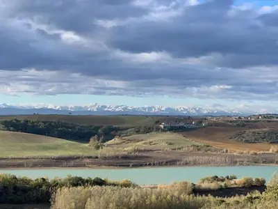 a lake in the middle of a field with snow covered mountains at La bergerie - Paisible vue lac et montagne in Molleville