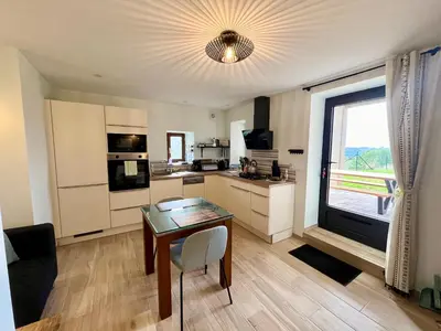 a living room with a table and a kitchen with a window at La bergerie - Paisible vue lac et montagne in Molleville