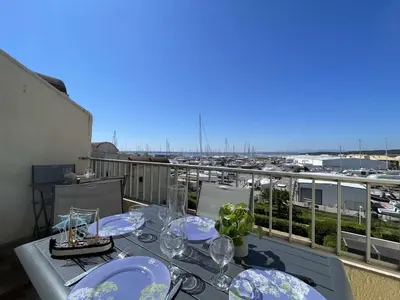 a table with glasses on a balcony with a view of a harbor at Appartement climatisé résidence Grande Voile GN160-434 in Gruissan