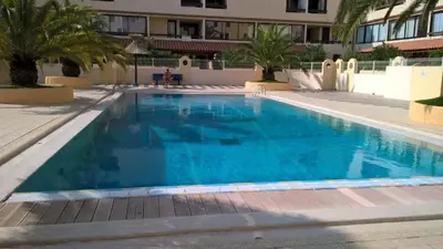 a large blue swimming pool with palm trees and a building at Vue sur les voiliers in Gruissan
