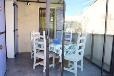 a table and chairs on a balcony with a glass door at Pavillon Cosy 3 pièces avec véranda et parking GN520-048 in Gruissan