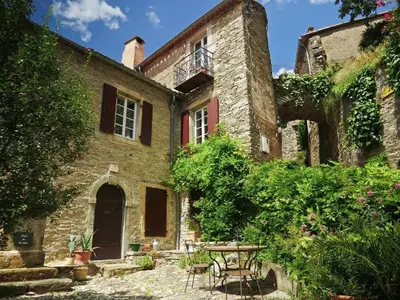 an old stone house with a table and chairs at Ostal de la Croix Vieussan in Vieussan