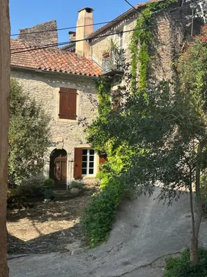 an old stone house with a tree in front of it at Ostal de la Croix Vieussan in Vieussan