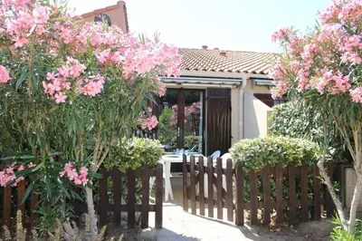 a wooden fence in front of a house with pink flowers at Maison studio mezzanine avec parking privé GN020-095 in Gruissan