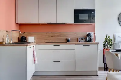a kitchen with white cabinets and an orange wall at Chez Seb - Raffiné et Accueillant in Carcassonne