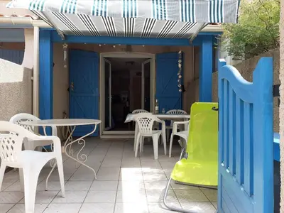 a patio with white tables and chairs and a blue door at Maison climatisée à 20m du bras de mer GA070-040 in Gruissan