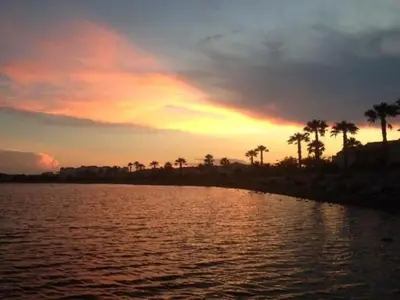 a sunset over a body of water with palm trees at Maison climatisée à 20m du bras de mer GA070-040 in Gruissan