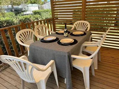 a table with chairs and a bottle of wine on a deck at Mobil-home 3 ch camping TOHAPI in Port-la-Nouvelle