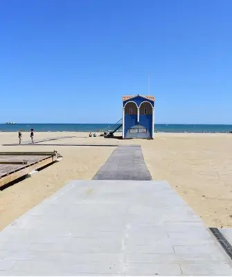 a boardwalk on a beach with a blue building at Mobil-home Port la Nouvelle in Port-la-Nouvelle
