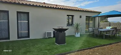 a backyard with a lawn with a grill and an umbrella at Villa moderne avec piscine privée in Roubia