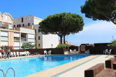 a swimming pool with tables and chairs next to a building at Appartement avec grande terrasse vue panoramique GN400-024 in Gruissan