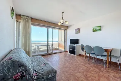 a living room with a couch and a table with chairs at Charming T2 with terrace on the seafront in Port-la-Nouvelle