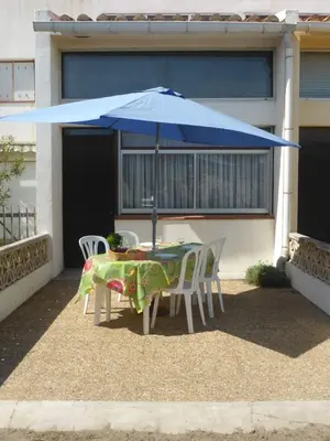 a table and chairs with a blue umbrella in front of a house at Bright Family Home Near the Sea in Port-la-Nouvelle