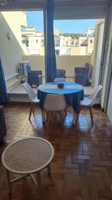 a table and chairs in a room with a balcony at Le Quai401 YourHostHelper in Gruissan