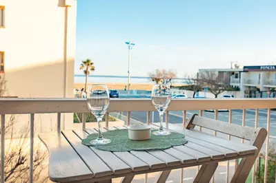 a table with wine glasses on a balcony with the beach at Les Jacinthes - Spacious sea view in Port-la-Nouvelle