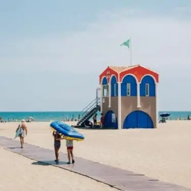 a couple of people walking on the beach with a surfboard at LE LOGIS, T2 au pied de la plage, Climatisation in Port-la-Nouvelle