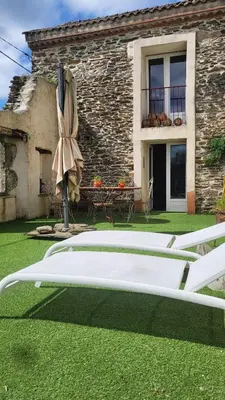 a patio with a bed and an umbrella and a building at La Maison du chataignier in Cassagnolles