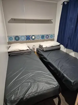 two twin beds in a room with blue curtains at Mobil-home Climatisé 6 personnes à Port La Nouvelle in Port-la-Nouvelle