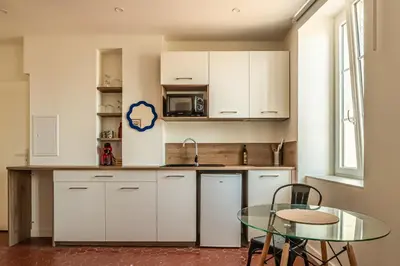 a kitchen with white cabinets and a glass table at Studio Blue Délice in Narbonne