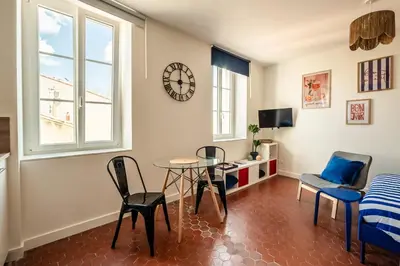 a living room with a table and chairs and a clock at Studio Blue Délice in Narbonne