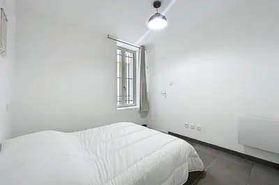 a white bedroom with a bed and a window at T2 apartment in the heart of Cuxac-d'Aude in Cuxac-dʼAude