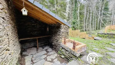 a stone building with a wooden roof and a bench at Le moulin de cameliere in Caudebronde