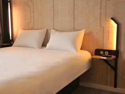 a bed with white sheets and a nightstand with a clock at B&B HOTEL Carcassonne Rocadest La Cité in Carcassonne