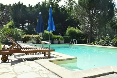 a swimming pool with two chairs and a blue umbrella at Aux portes du Sidobre in Burlats