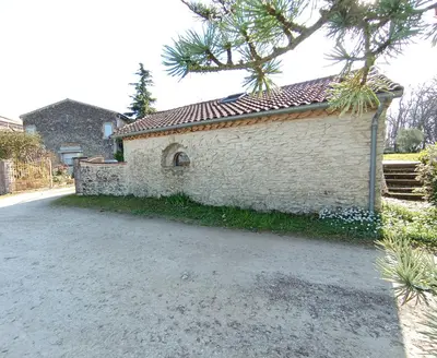 a white brick building with a tree next to a street at La maison au bout de l'allée in Carbes