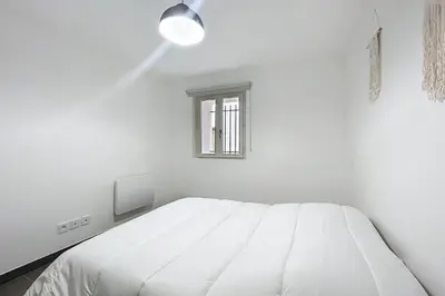 a white bedroom with a bed and a window at Bright T3 for 4 people in Cuxac-dʼAude