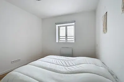 a white bedroom with a bed with a window at T3 apartment in the heart of Cuxac-d'Aude in Cuxac-dʼAude